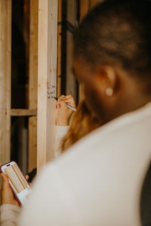Woman writing a message on wooden beam framing inside a home under construction.