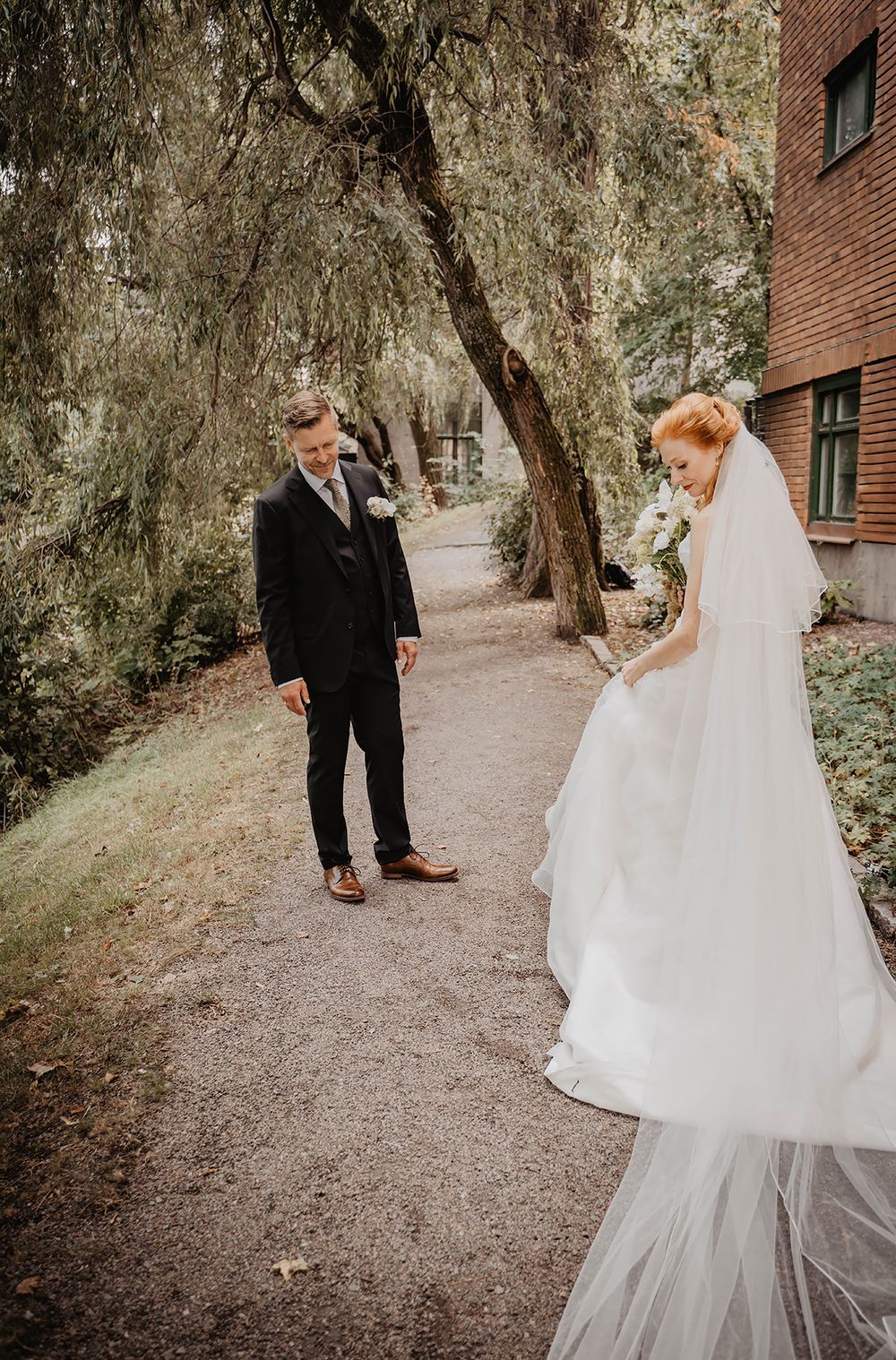 Brudgummen betraktar kärleksfullt sin blivande brud under en first look fotografering i Norrköping intill Strömsparken.