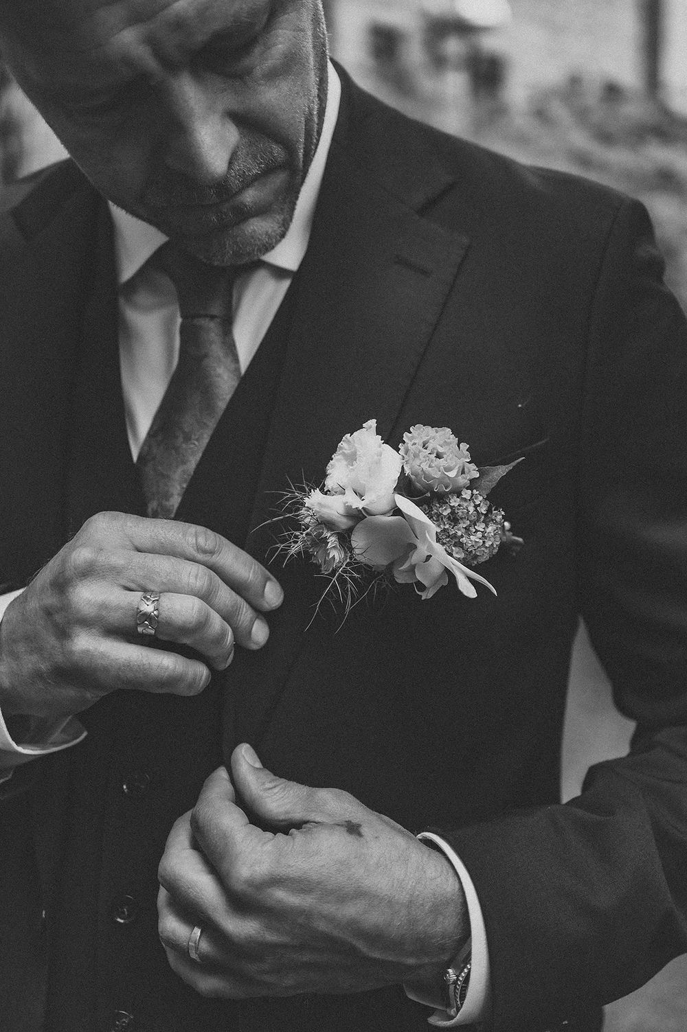 Detaljfoto i svartvit från bröllopsfotografering i Norrköping, där brudgummen rättar till sin kavaj och corsage.
