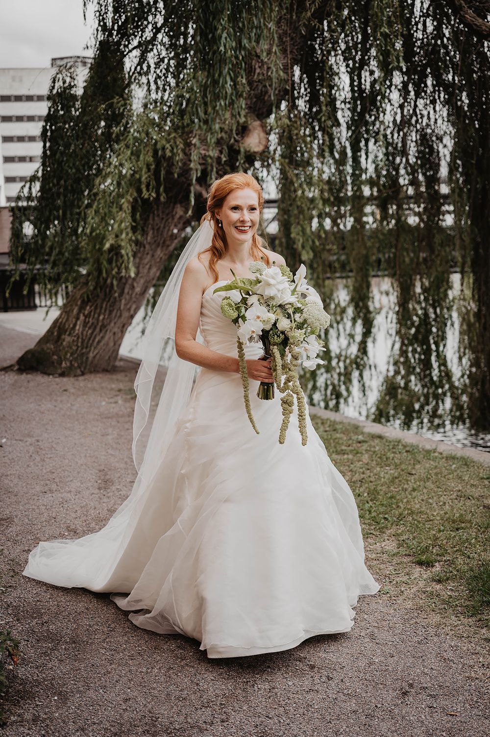 Brudporträtt i Strömsparken i Norrköping, där bruden bär lång vit brudklänning, brudslöja och vit brudbukett. Foto av Lets Bloom Media.