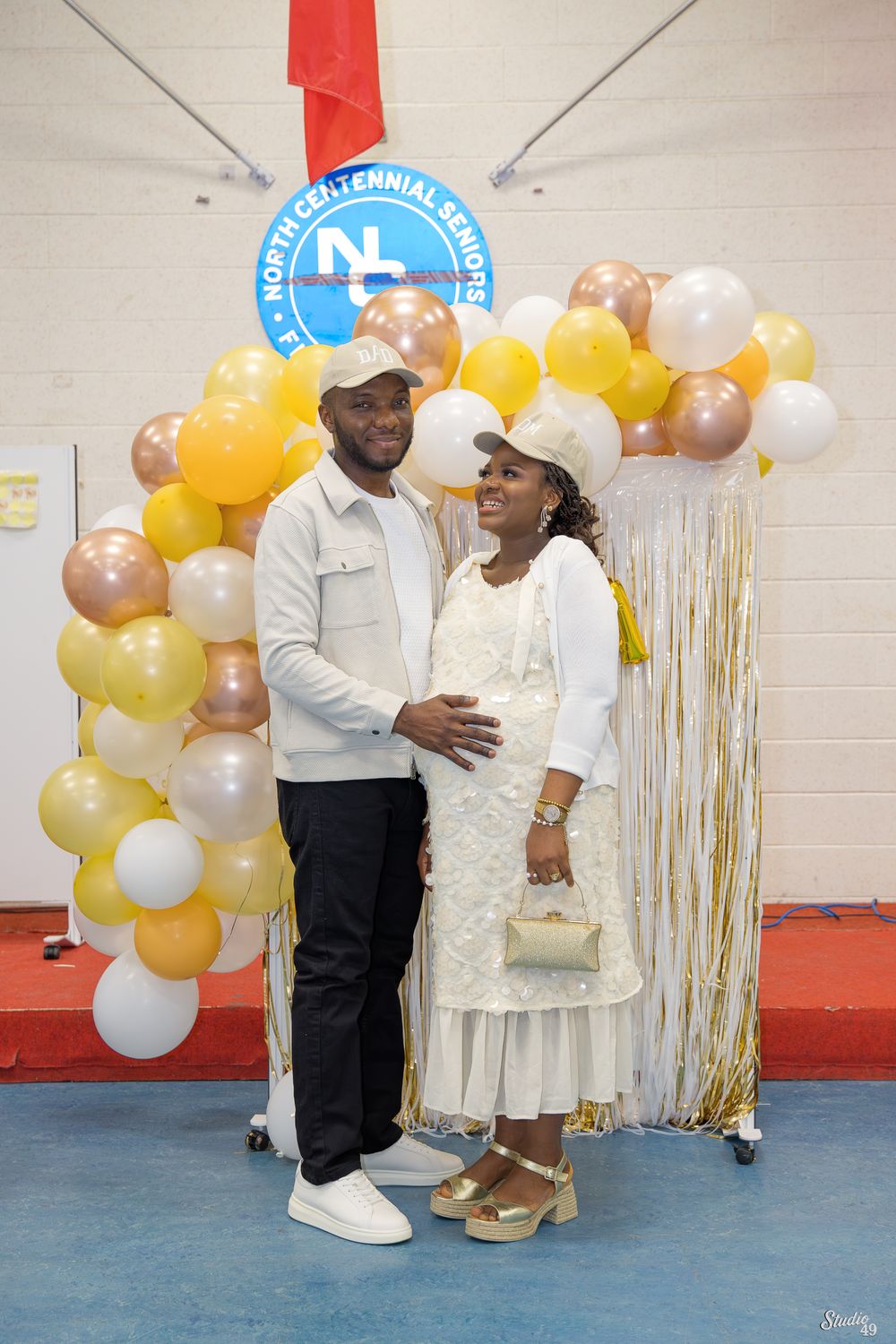 A couple poses together in front of a colorful balloon arch at a North Centennial Seniors community event indoors.