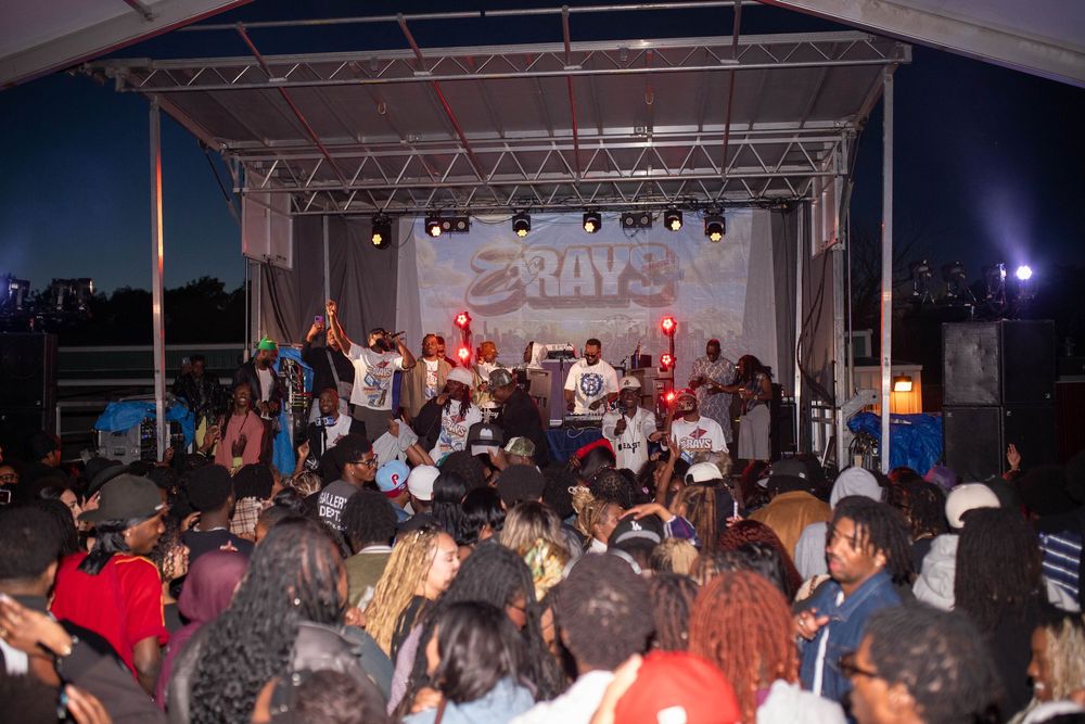 A large crowd enjoys a live outdoor concert performance on a lit stage at night during a community music event.