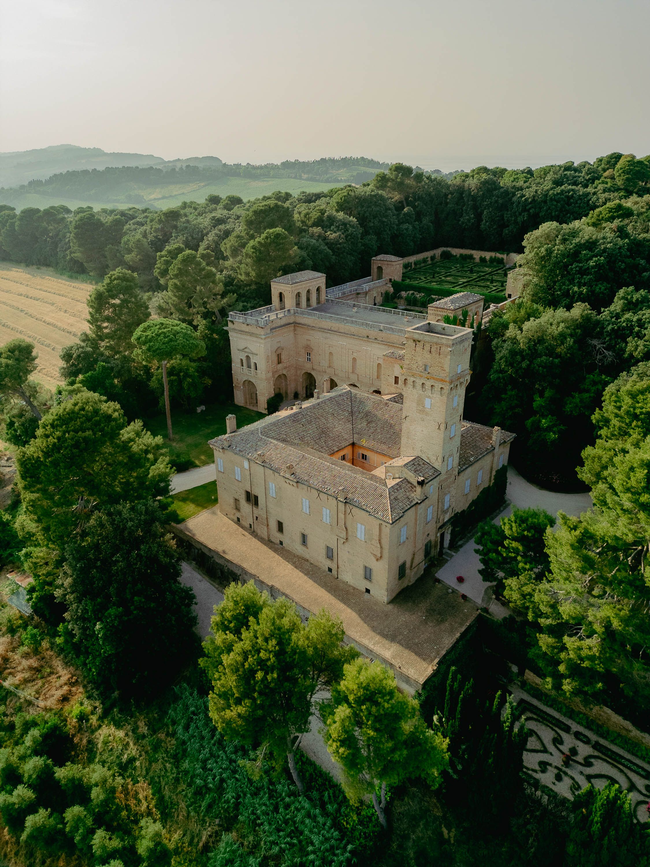 Aerial view of a historic Italian villa Imperiale Pesaro surrounded by lush green trees and manicured gardens in the countryside.