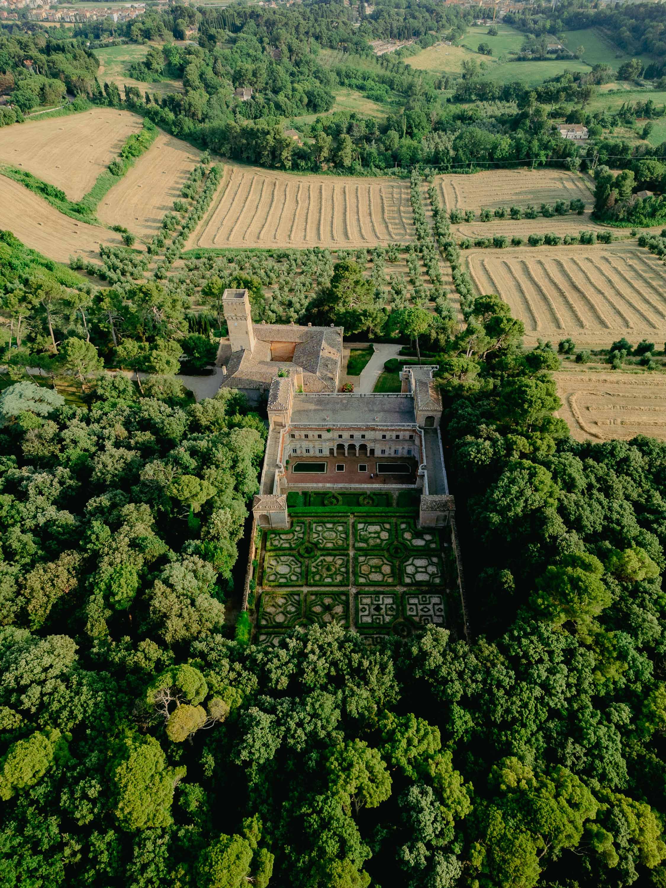 Aerial view of a historic Italian villa Imperiale, Pesaro with formal gardens, surrounded by lush trees and farmland fields.