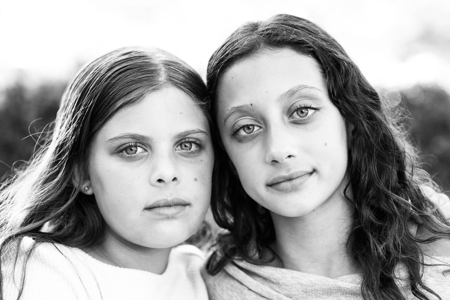 Black and white photo of a curious little girl peeking over a wooden fence with wide, expressive eyes.