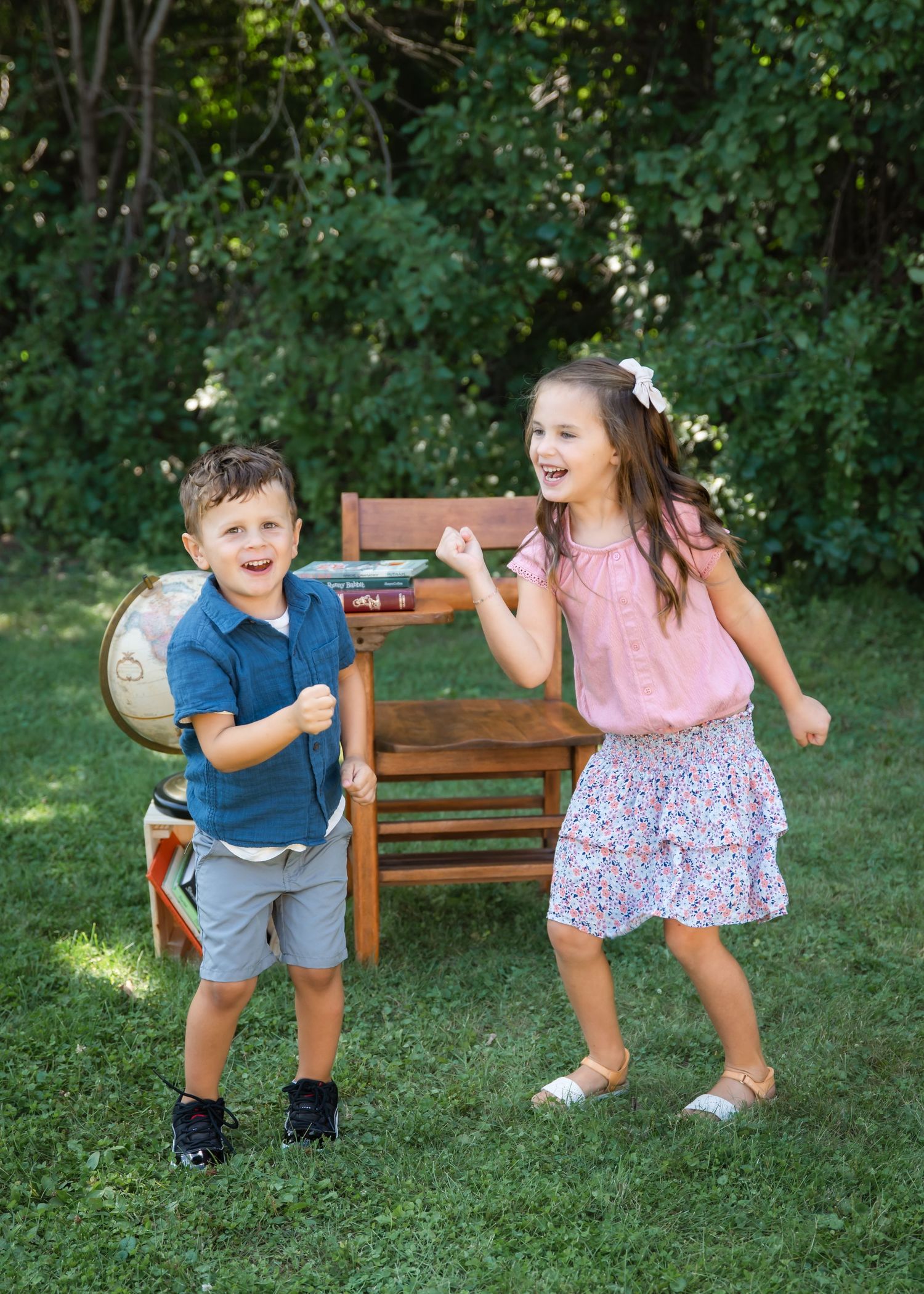 Two happy children dancing on green grass outdoors, boy in blue polo and girl in pink top with floral skirt.