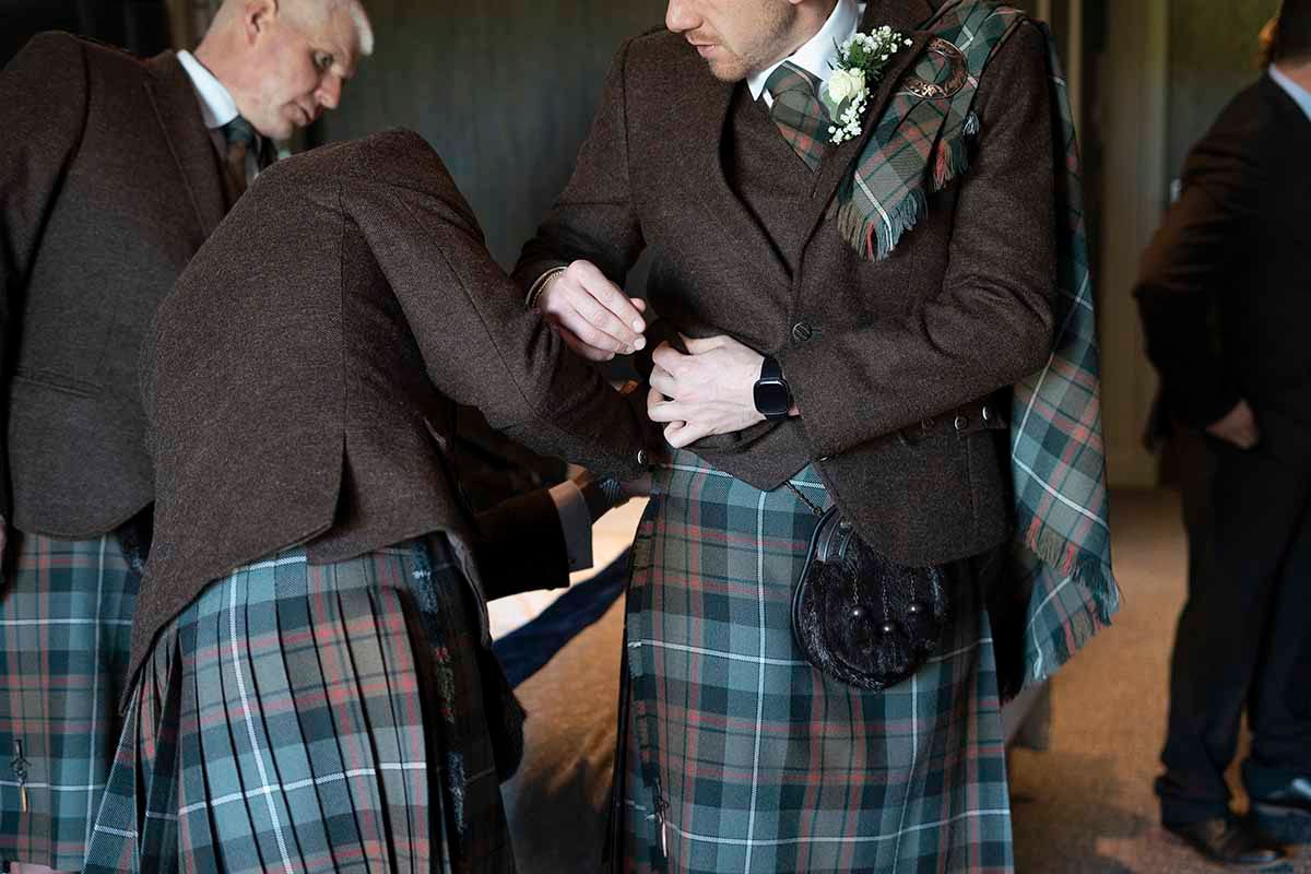 Men wearing traditional Scottish kilts in tartan patterns at a formal event.