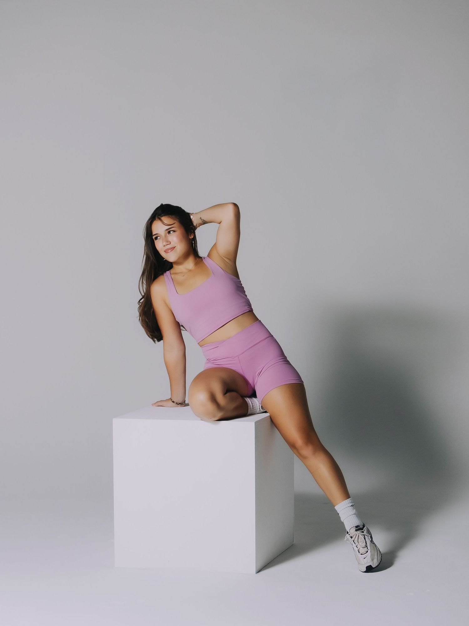 Studio fashion portrait of a woman in a pink outfit posing on a white cube