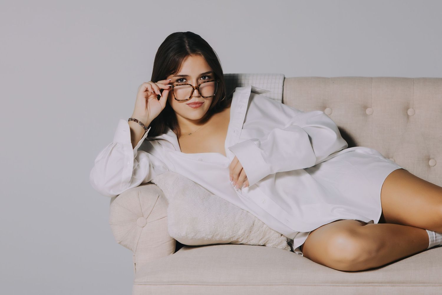 Studio portrait of a woman lounging on a couch in an oversized white shirt
