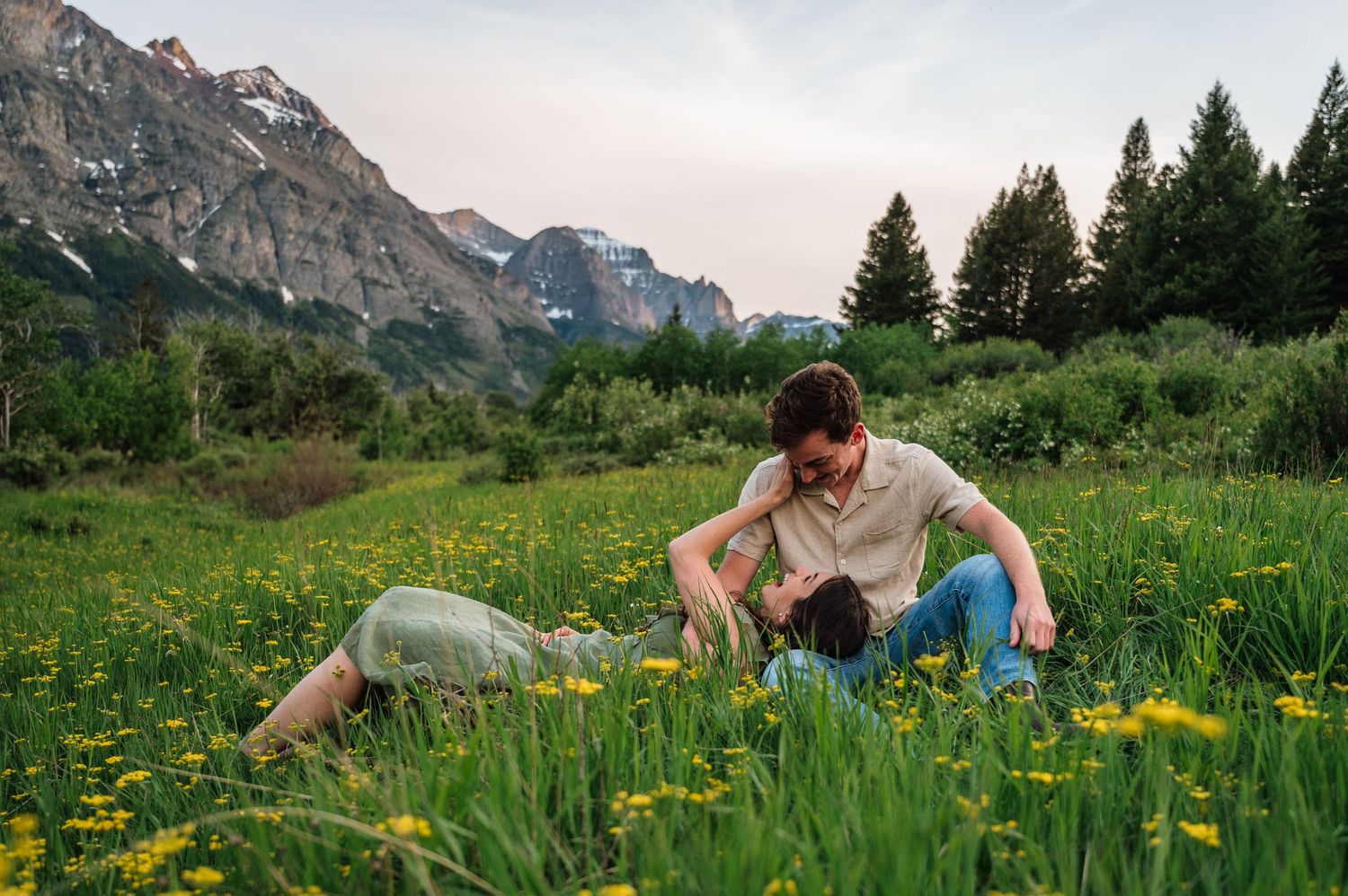 Couple sitting in a wildflower meadow with mountain backdrop at sunset.