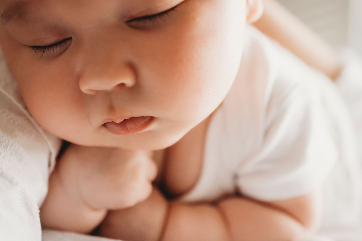 Close up of an infant in white clothing resting peacefully.