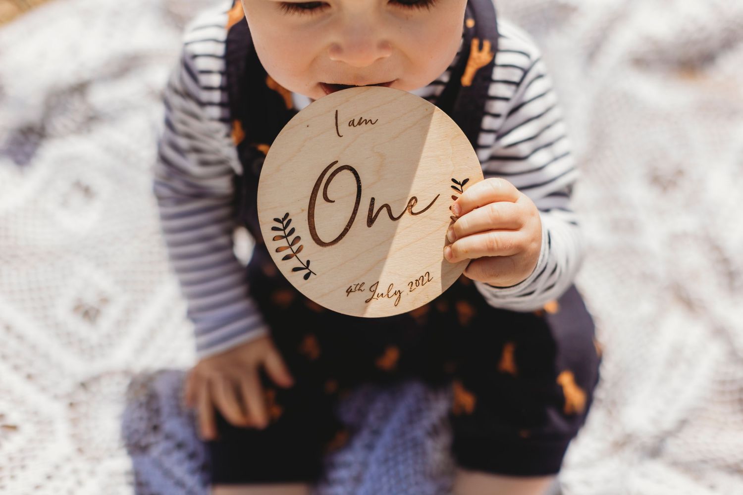 Small child in striped shirt holding a wooden disc with 'One' engraved on it against a white background.
