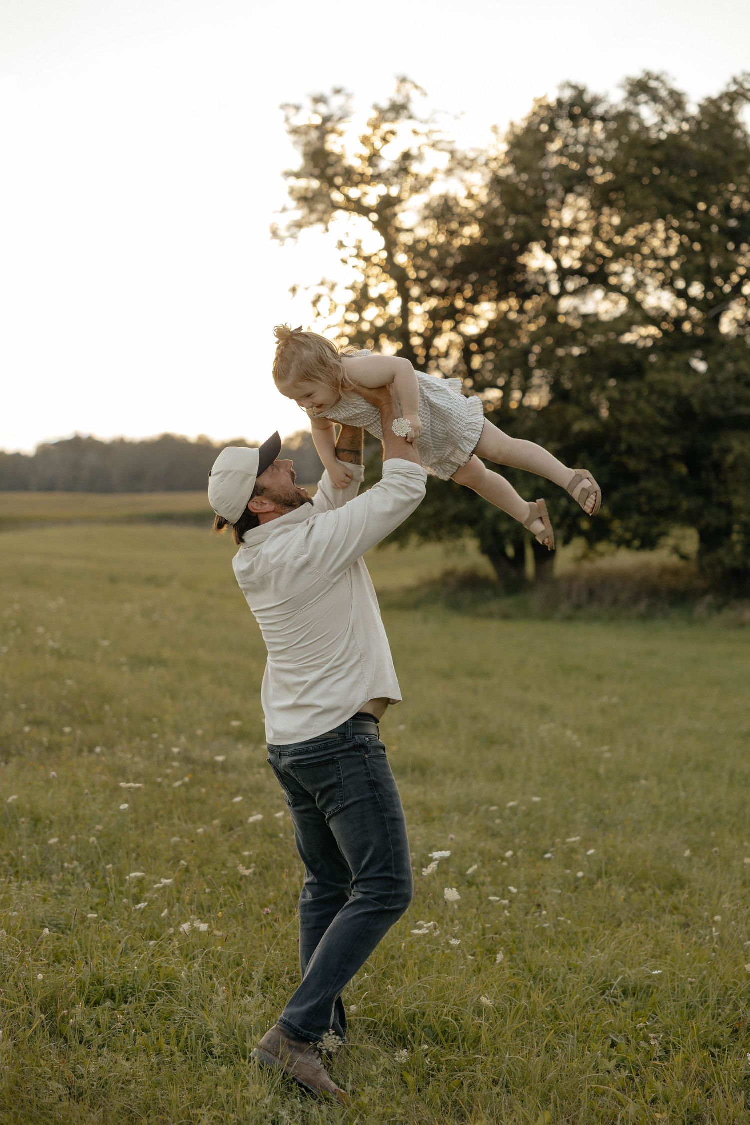 Father joyfully lifting his young daughter in a sunlit green field at golden hour.