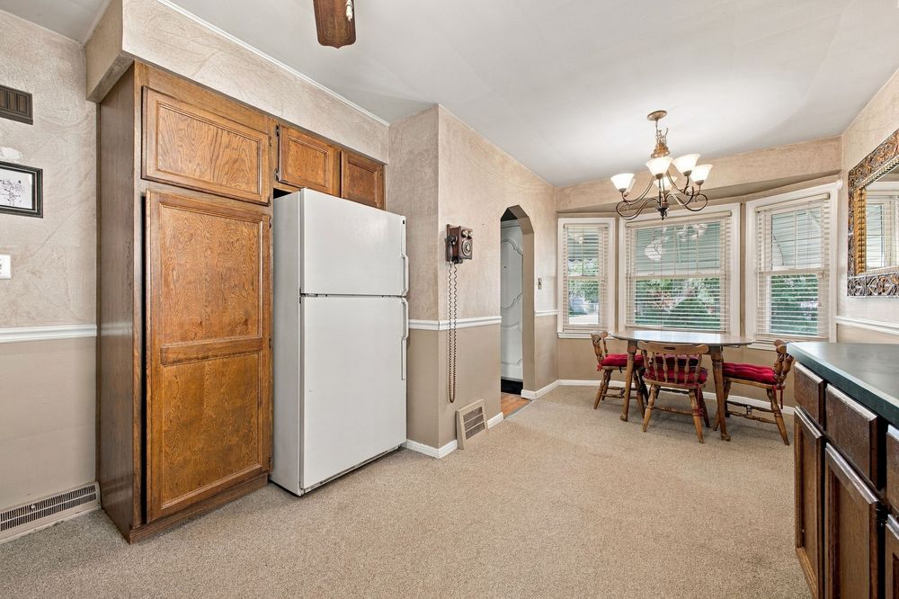 Kitchen with white refrigerator, wood cabinets, and dining area featuring a chandelier and natural light from windows.