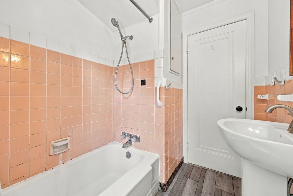 Vintage bathroom with pink tiles, white bathtub, shower, pedestal sink, and wood-effect flooring.