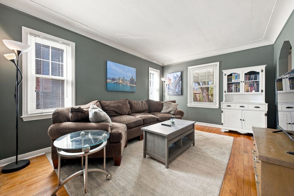 Cozy living room with gray sectional sofa, glass coffee table, hardwood floors, and white hutch cabinet against sage green walls.