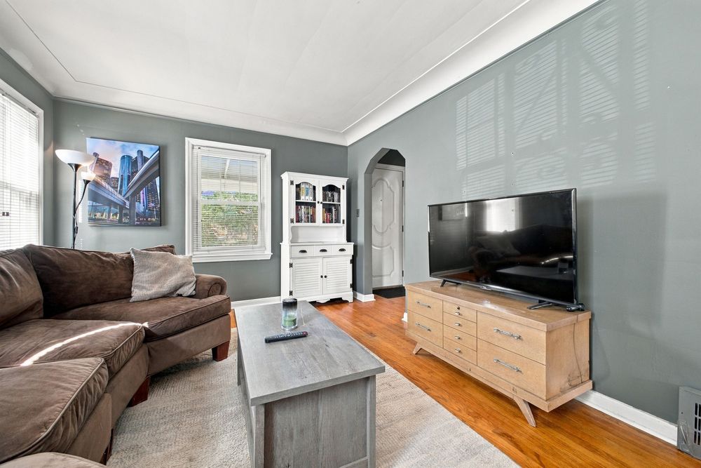 Cozy living room with gray walls, hardwood floors, brown sofa, light wood TV stand, and white arched doorway.
