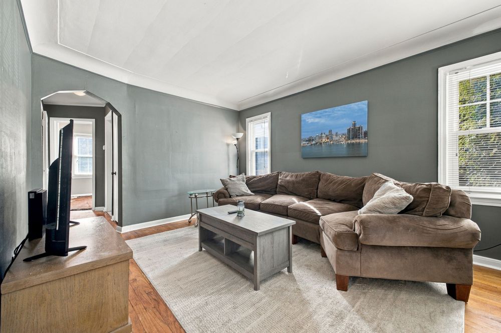 Cozy living room with brown sectional sofa, gray coffee table, hardwood floors, and city skyline artwork on blue-gray walls.