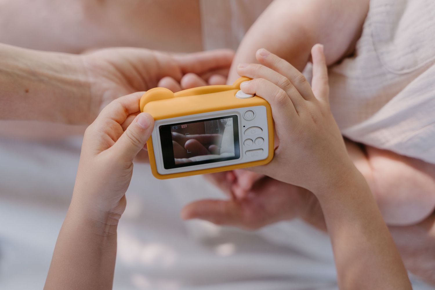 Child and adult hands holding a small yellow toy camera with screen displaying a photo.