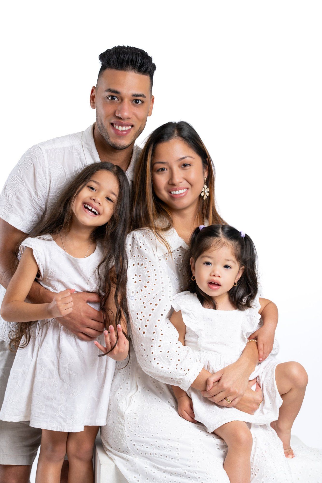 Happy mixed-race family of four posing in matching white outfits against a white background in a studio portrait.