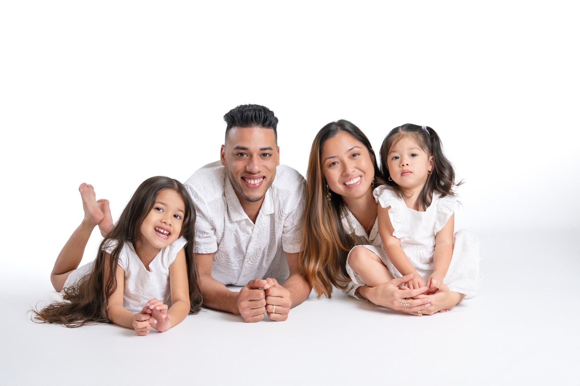 Happy Asian family of four posing together on white background, parents and two young daughters smiling.