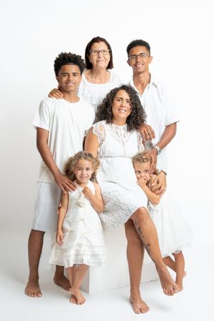Multi-generational family of six in white outfits posing together for a studio portrait photo.