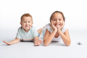Two smiling children lying on a white floor, a boy in a mint shirt and a girl in white, posing happily.