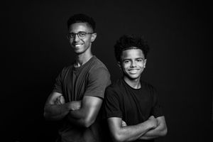 Black and white portrait of two young men posing back-to-back with arms crossed, smiling confidently.