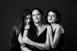 Black and white portrait of a mother embracing her two daughters in a studio setting.