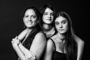 Black and white portrait of three women posing together against a dark background.