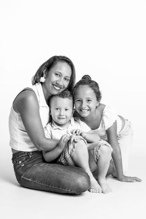 Black and white portrait of a smiling mother with her two children sitting together on a white background.