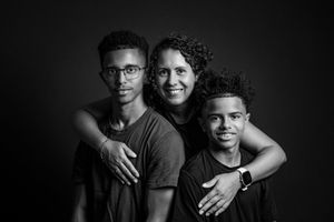 Black and white studio portrait of a mother with her two sons, smiling warmly against a dark background.