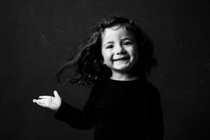 Black and white portrait of a smiling young girl with curly hair wearing a black top, posing playfully.