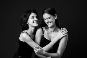 Two young women laughing and embracing in a black and white studio portrait photo.