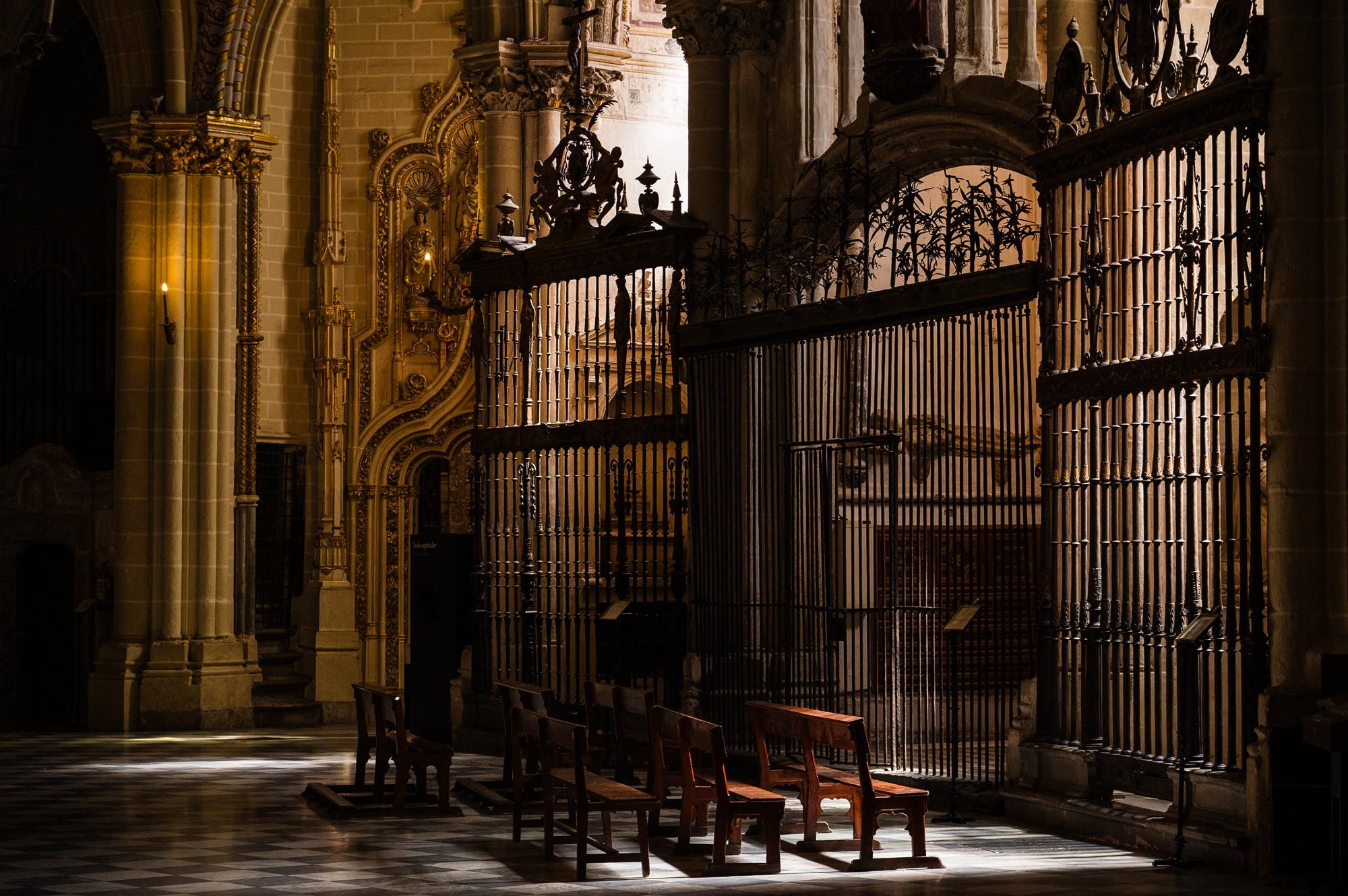 Dimly lit cathedral interior with ornate iron gates, wooden pews, and dramatic light streaming through Gothic arches.