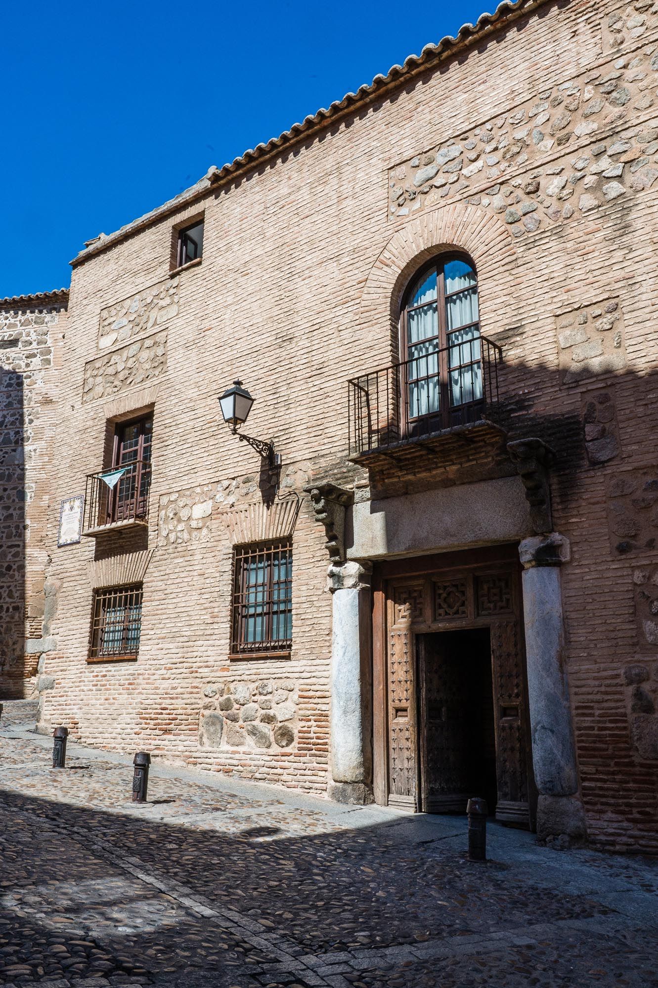 Historic brick building with ornate doorway and arched windows on a cobblestone street in Toledo, Spain.