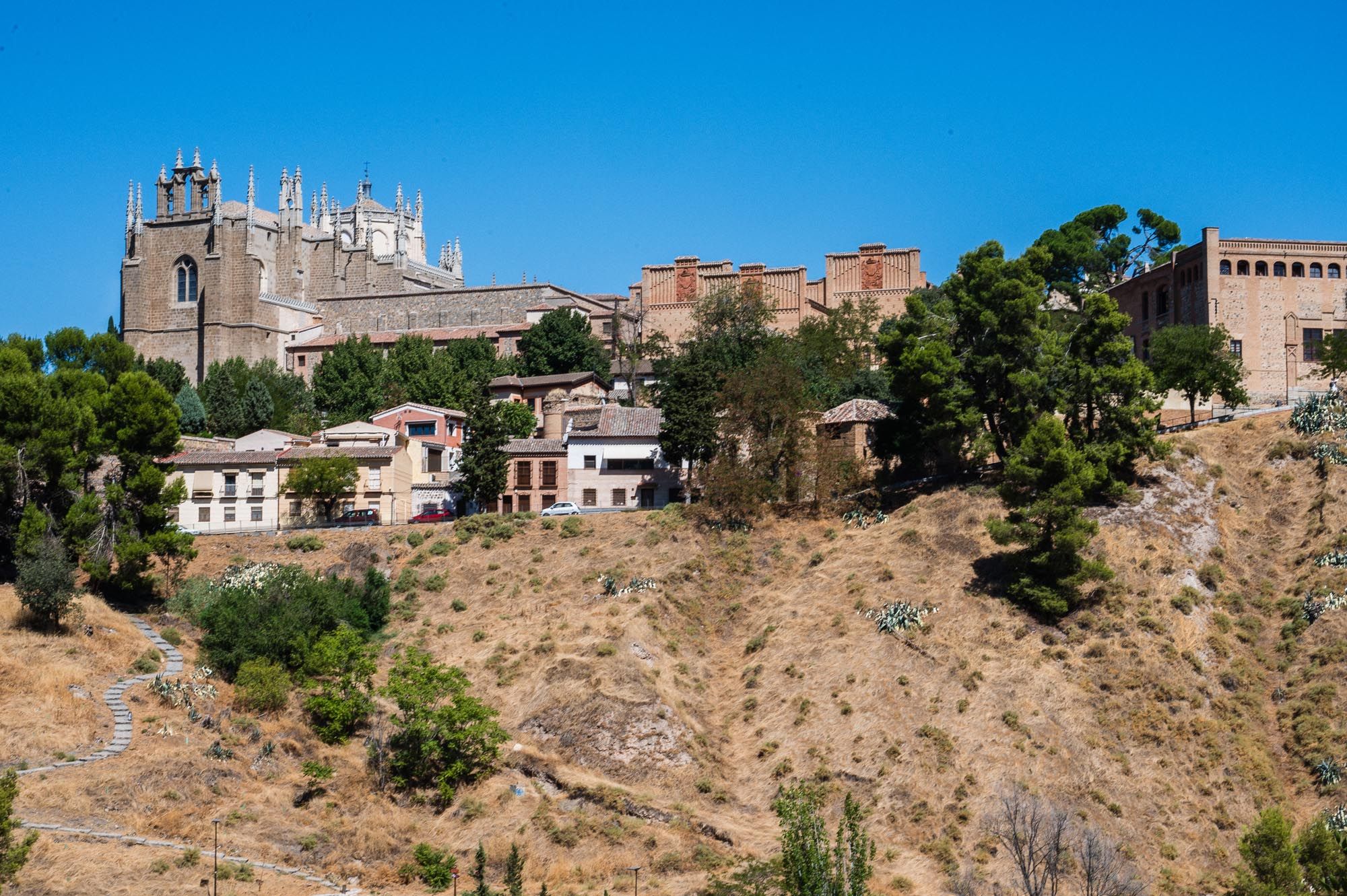 Historic hilltop town of Toledo, Spain, with medieval cathedral and stone buildings under a clear blue sky.
