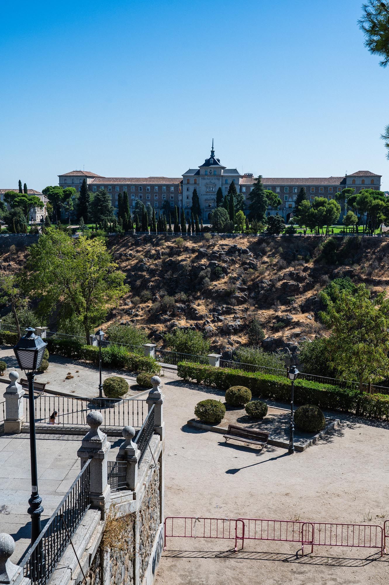Historic Spanish building on a hill surrounded by cypress trees, with manicured gardens and stone balustrade in Toledo, Spain.