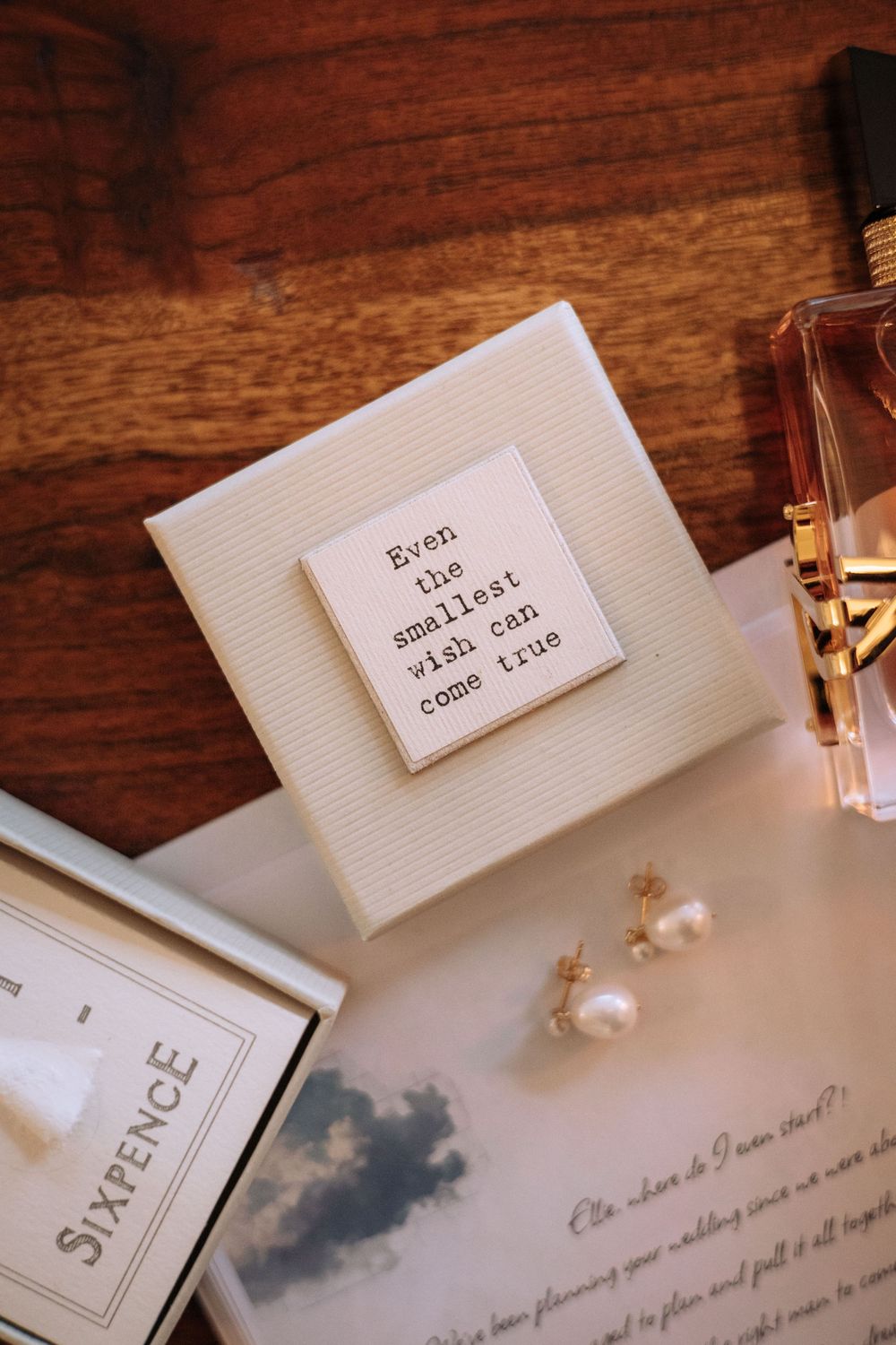 Wedding flat lay with gift box reading 'Even the smallest wish can come true', pearl earrings, sixpence, and perfume.