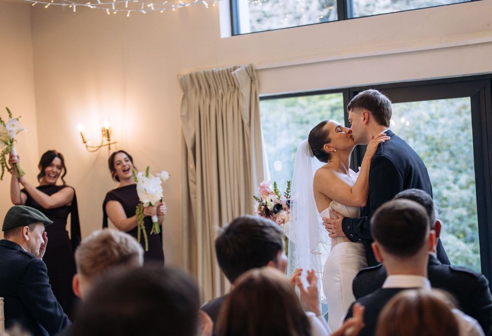 Newlyweds share first kiss surrounded by cheering guests in a beautifully decorated wedding venue.