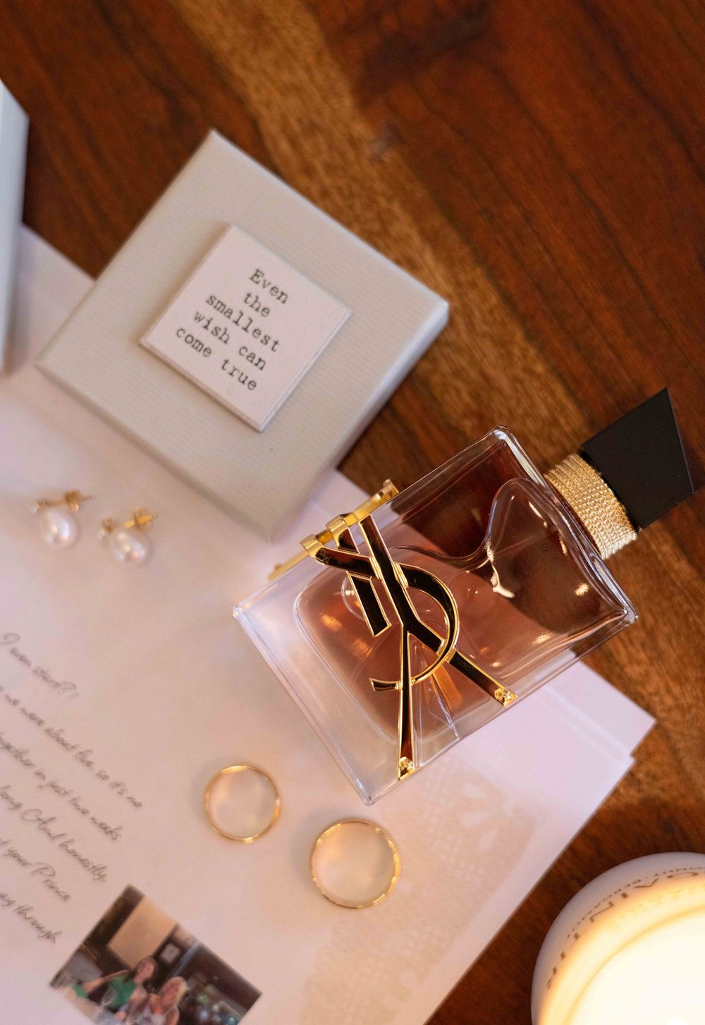 YSL Libre perfume bottle with gold accents beside pearl earrings and rings on a wooden surface.