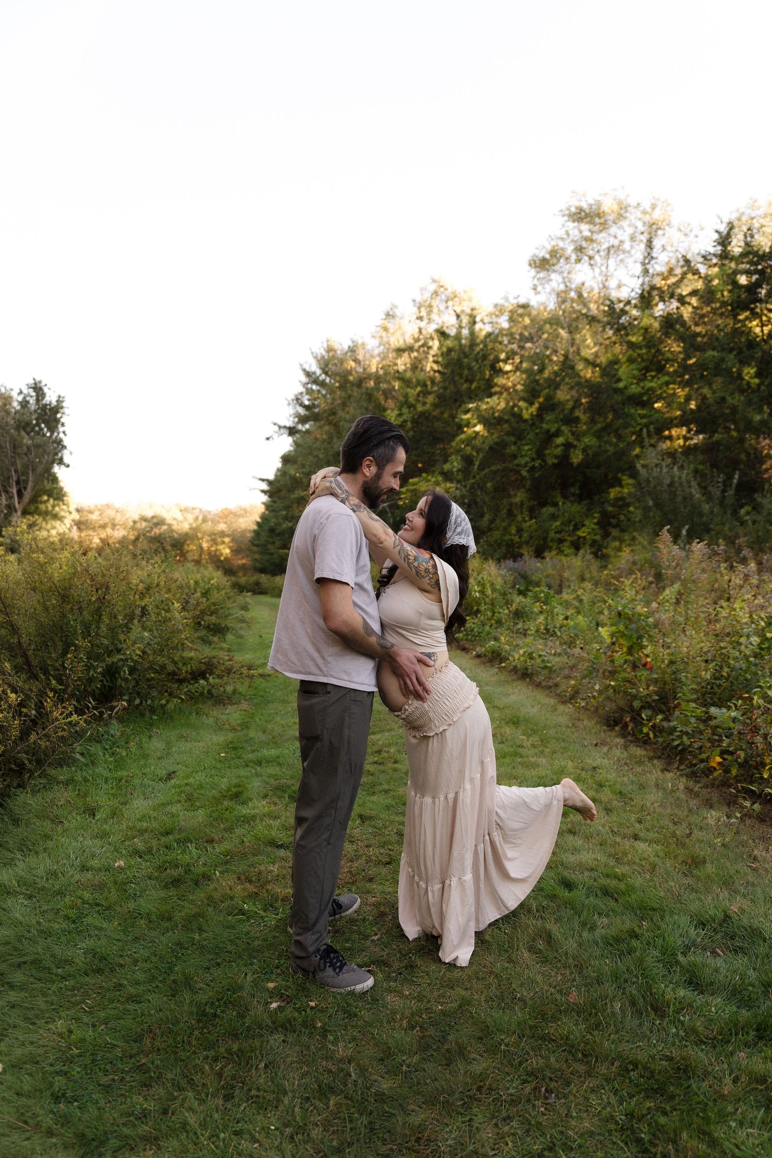 Tattooed bride and groom sharing a joyful kiss in a green field at their outdoor wedding.