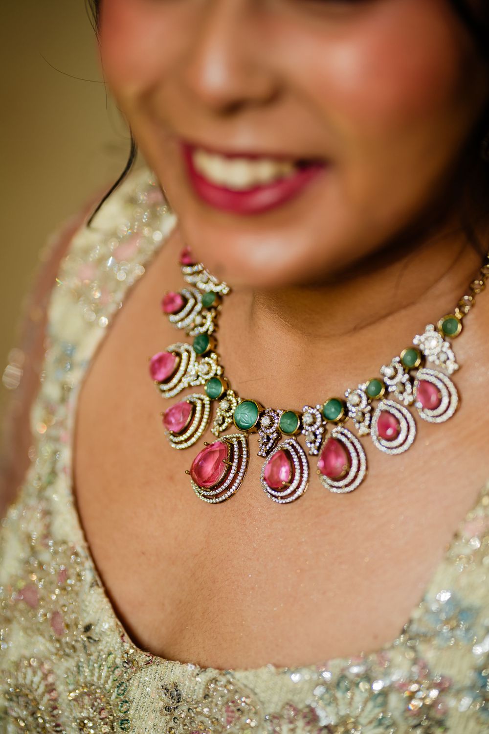 Smiling bride wearing an elegant necklace with pink gemstones and emeralds, paired with an embroidered ivory lehenga.