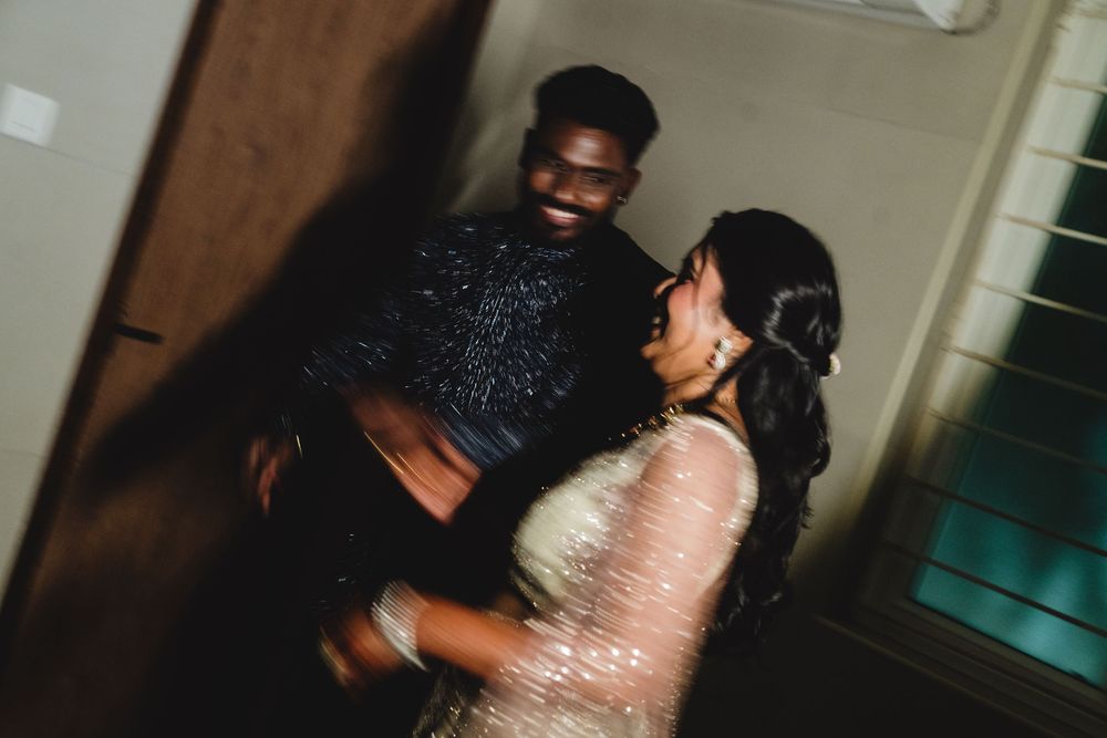 A joyful couple dancing together, the man in a black sequin shirt and woman in a shimmery saree, sharing a romantic moment.