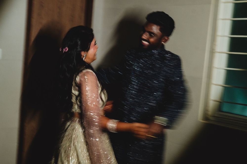 Couple shares a joyful laughing moment indoors, groom in dark sherwani, bride in embroidered lehenga.