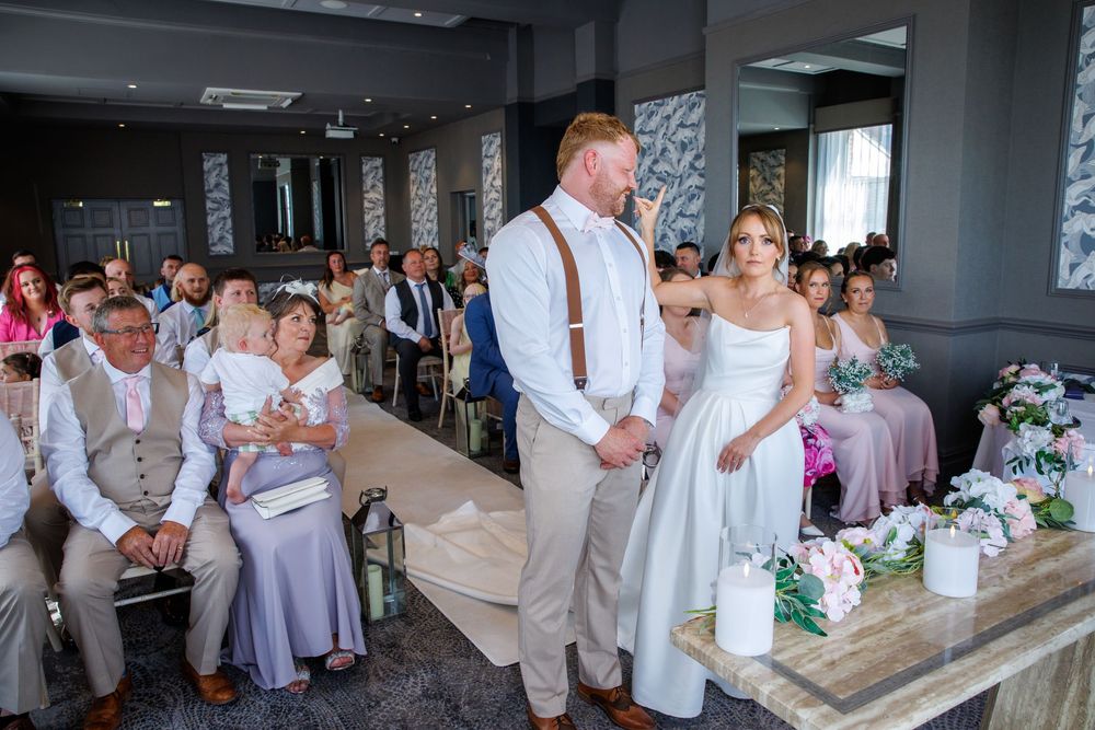 Bride and groom stand at the altar during an indoor wedding ceremony with guests seated in rows behind them.