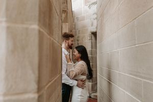 Couple embracing romantically in a narrow stone corridor, dressed in elegant wedding attire.