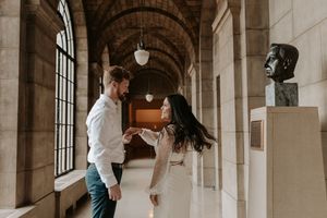 Couple dancing and holding hands in an elegant arched hallway with stone columns and a bronze bust sculpture.