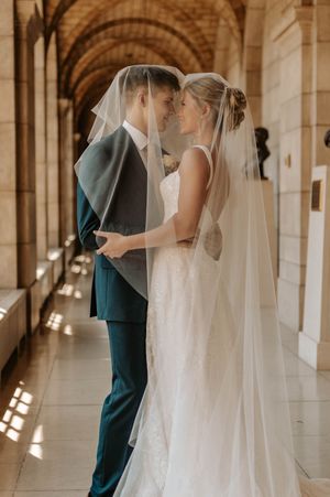 Bride and groom share an intimate moment under a veil in an elegant arched hallway on their wedding day.