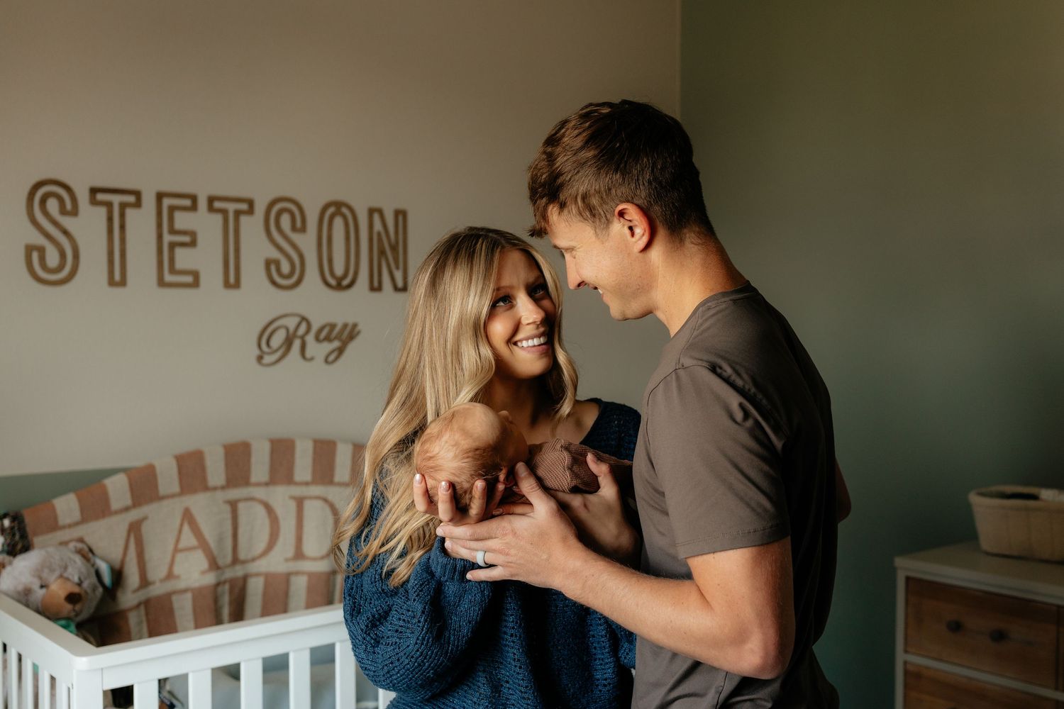 Couple smiling together in a nursery with Stetson Ray name sign on green wall beside a white crib.